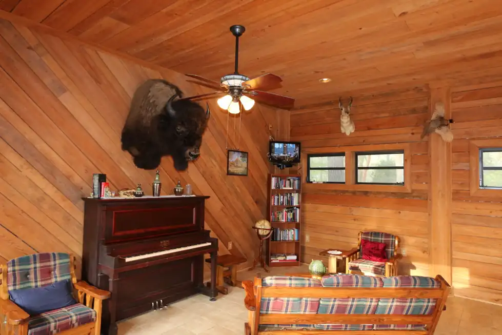 Pine-paneled clubhouse lounge with an upright piano, a bison mount and plaid armchairs