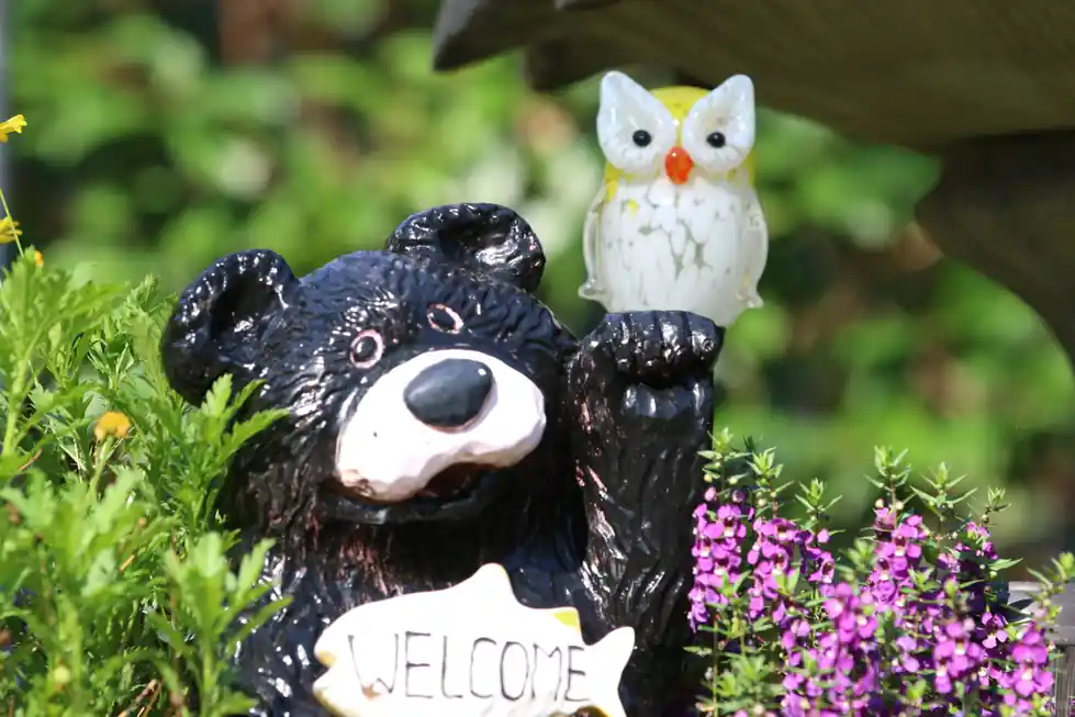 Carved black bear holding a welcome sign among purple flowers